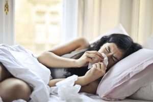 a young woman blows her nose in bed, suffering from the flu